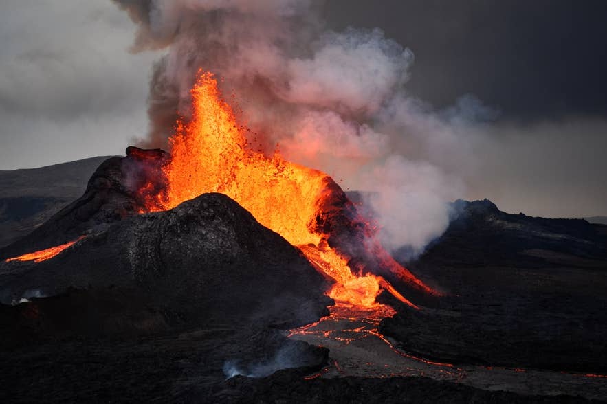 Uitbarsting van de Fagradalsfjall-vulkaan op het Reykjanes-schiereiland, met lava die uitbarst en over het donkere vulkanische terrein stroomt.
