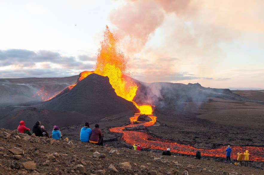 Een kleine vulkaanuitbarsting op het Reykjanes-schiereiland met lava die uitbarst en over het donkere, rotsachtige landschap stroomt.