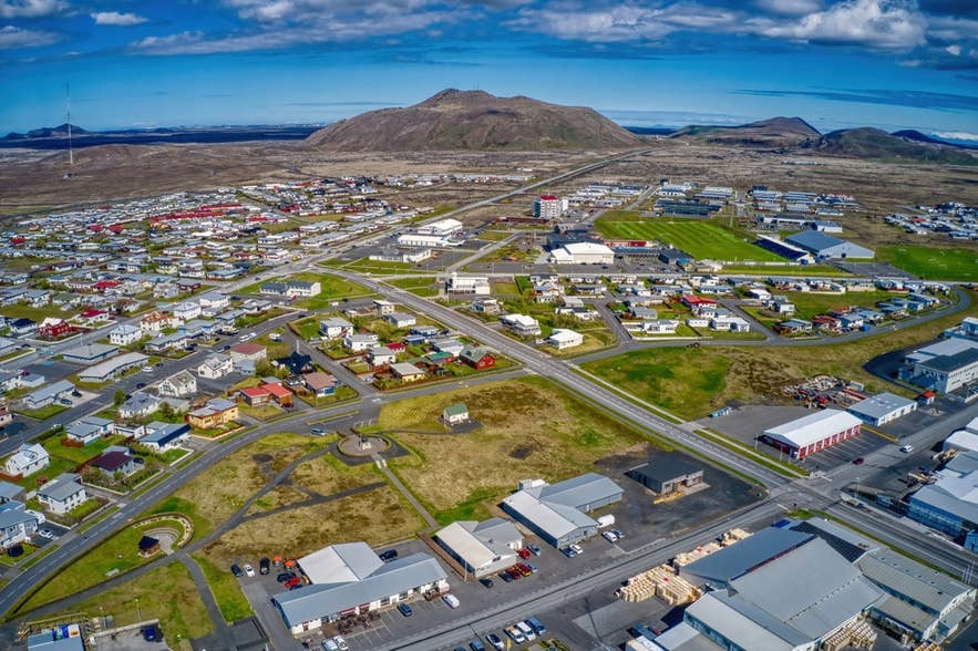 Luchtfoto van Grindavik, IJsland, met kleurrijke huizen, wegen en bergen onder een heldere blauwe lucht.