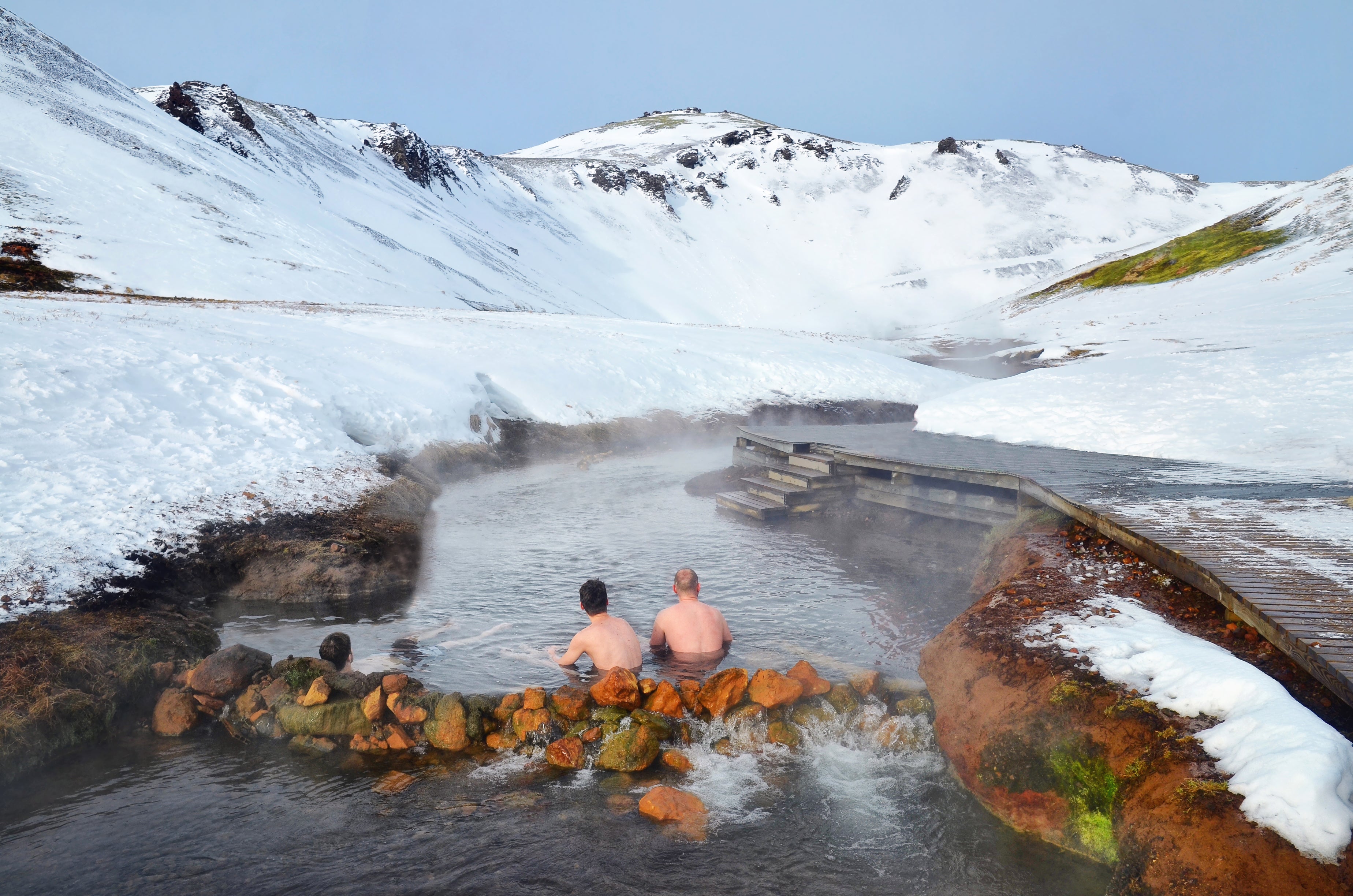 Two men enjoy a soak on Reykjadalur River surrounded by snowy landscapes on a Reykjaladur tour.