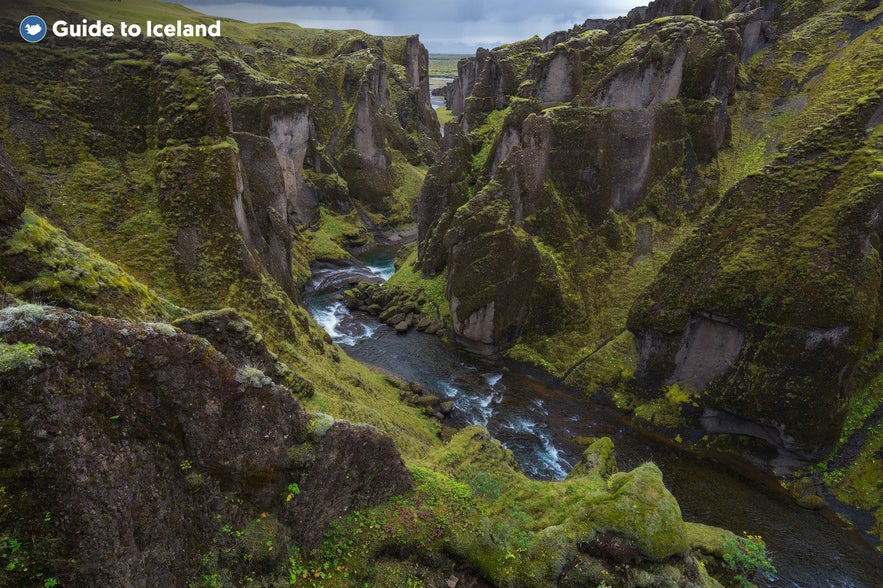 Aerial view of the mossy green Fjadargljufur canyon in South Iceland with a winding river flowing between steep cliffs.