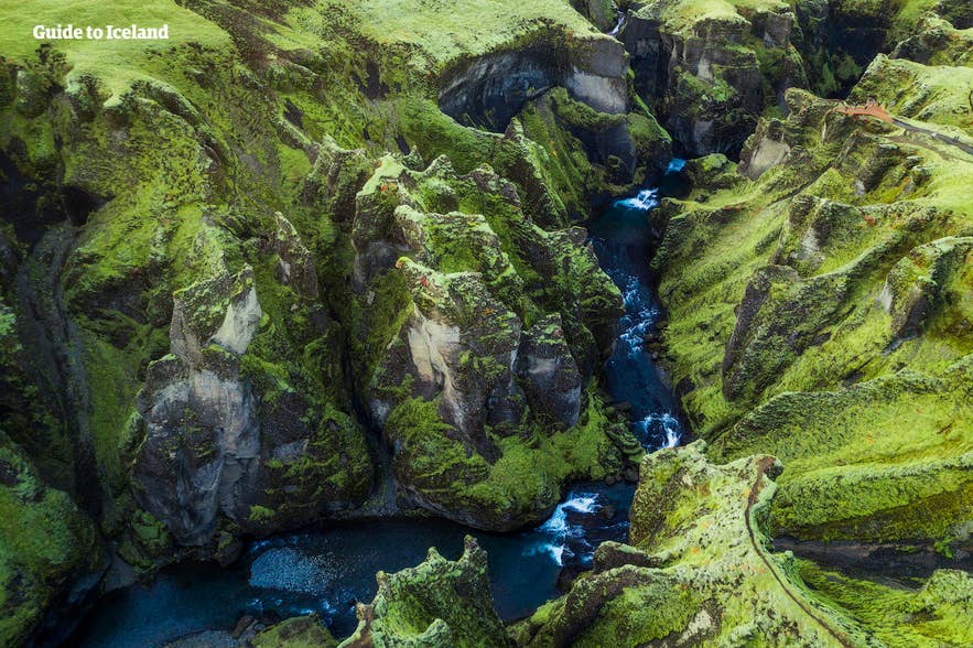 Aerial view of Fjadargljufur canyon in south Iceland, with a winding blue river cutting through steep moss-covered cliffs.