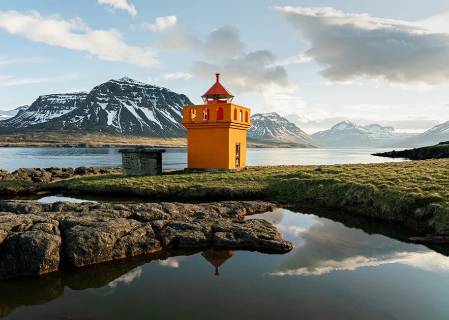 Brimnesviti lighthouse on a bright day with snowy mountains in the background.