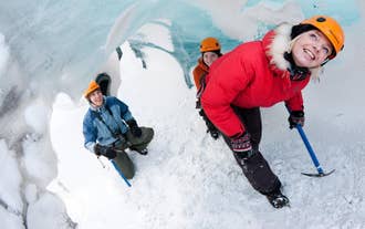 Tre turgåere utforsker en isgrotte under en fottur på Sólheimajökullbreen, med isøkser og hjelmer, omgitt av blå og hvite isvegger.