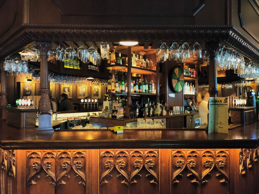 The Irishman Pub in Reykjavik with ornate wooden bar, hanging glasses, and shelves of liquor bottles.