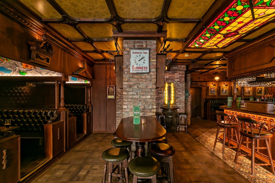 The Irishman Pub in Reykjavik featuring wooden bar, stained glass light, and cozy seating booths.