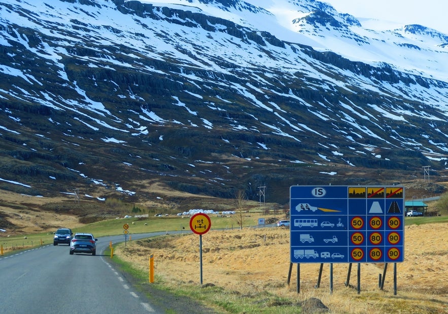 Mountain road in Seydisfjordur, Iceland, with speed limit signs and snowy peaks. Brimnesviti Lighthouse is located nearby.