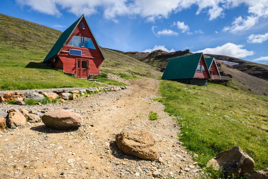 A gravel path leads to red A-frame cabins at the Kerlingarfjoll Mountain Resort, surrounded by green slopes and mountains.