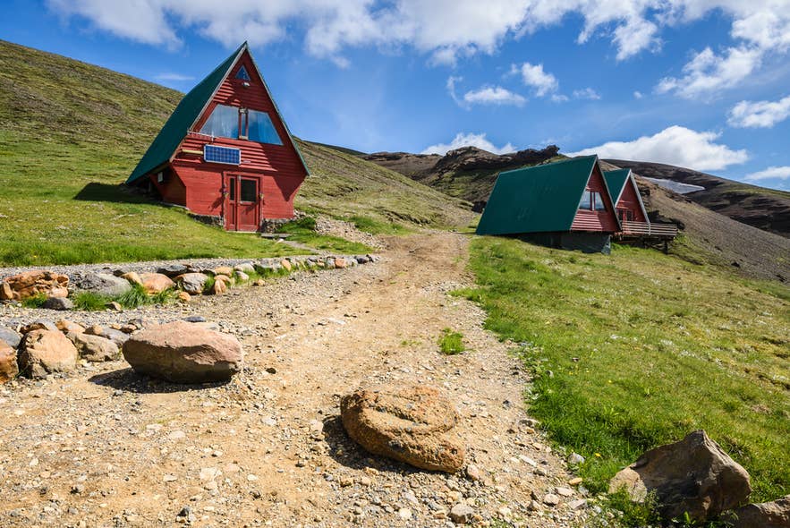 A gravel path leads to red A-frame cabins at the Kerlingarfjoll Mountain Resort, surrounded by green slopes and mountains.