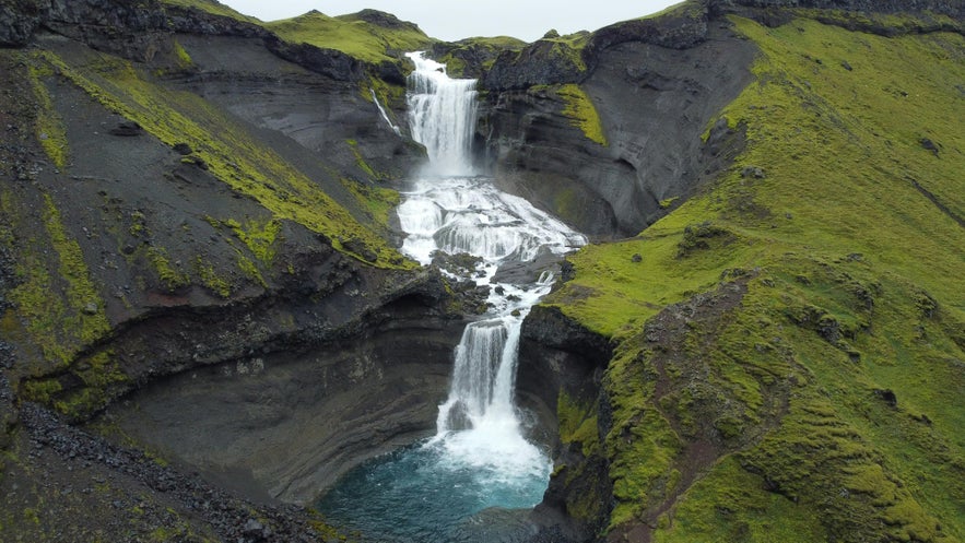 A waterfall cascading through Sigöldugljúfur canyon surrounded by lush green landscape.