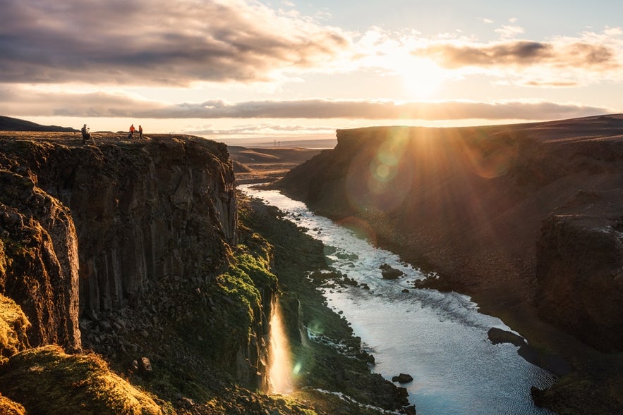Beautiful sunset over Sigoldugljufur with hikers standing on a cliff and waterfall flowing in gorge on Icelandic Highlands.