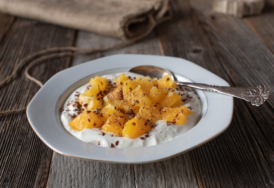 Skyr served with fresh orange slices and linseeds on a breakfast plate with a spoon.