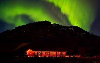 一座明亮的红色小屋矗立在南海岸，背后是巨大的山影，夜空中北极光闪耀。