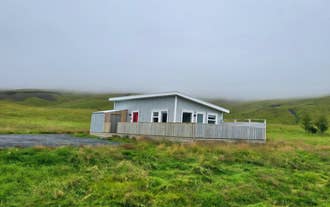 Un cottage azzurro recintato si trova al centro di un campo verde in una giornata nuvolosa, presso Seljalandsfoss Sky Retreat a Hvolsvöllur.