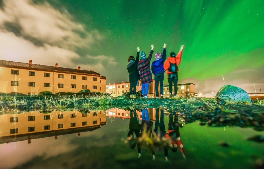 People looking at northern lights in Iceland in Asbru near Keflavik airport with reflection in the water