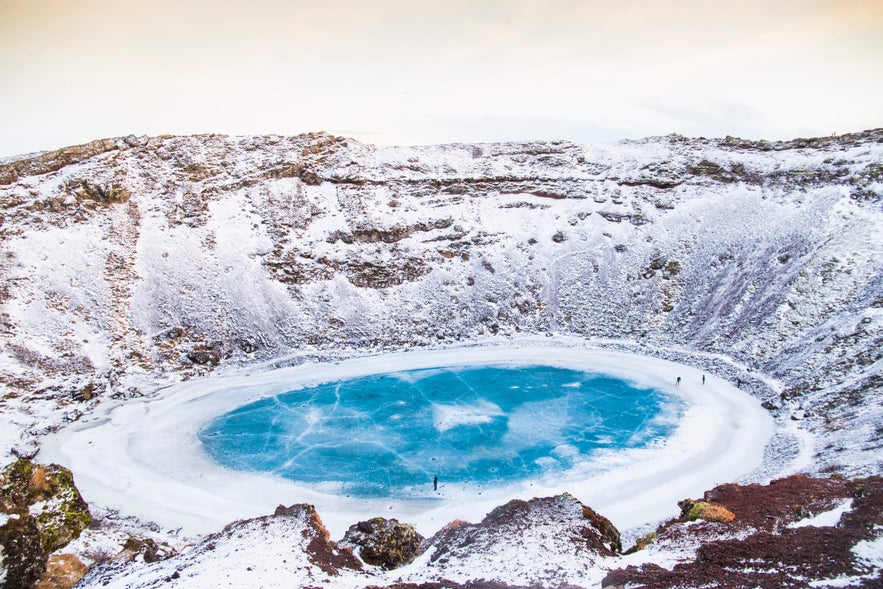 Kerid Crater in South Iceland is covered in snow, showing a stunning winter landscape with a frozen volcanic lake.